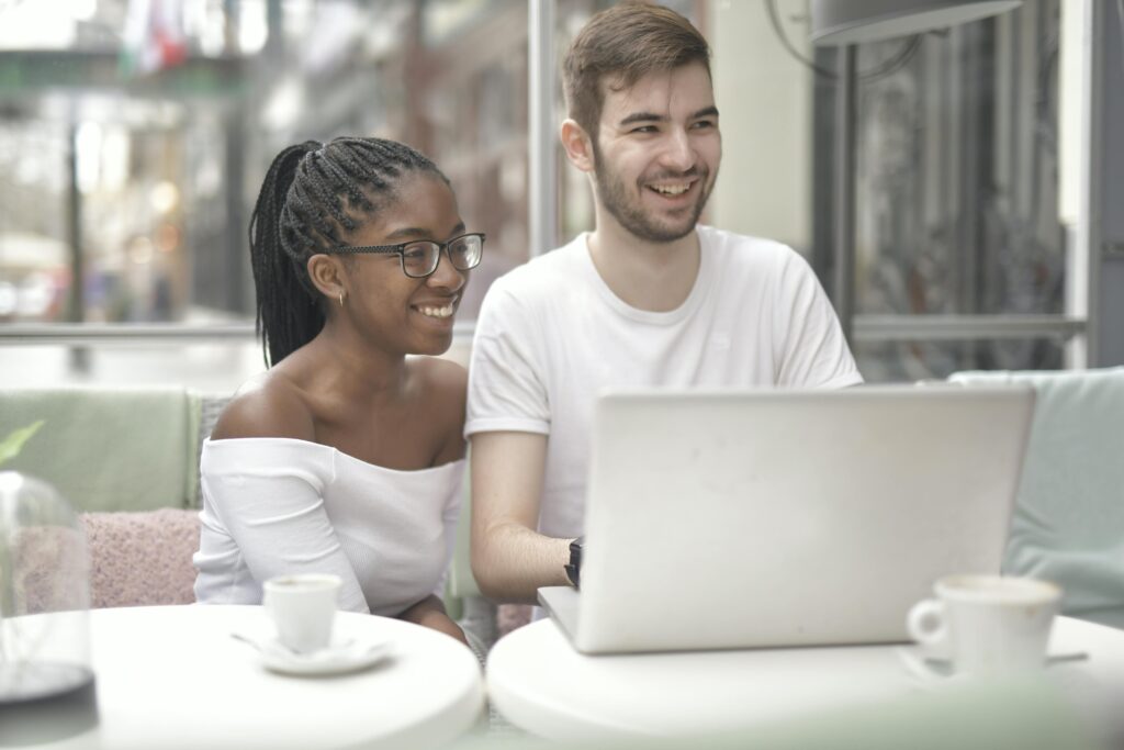Smiling couple enjoying coffee while using a laptop in a cafe.