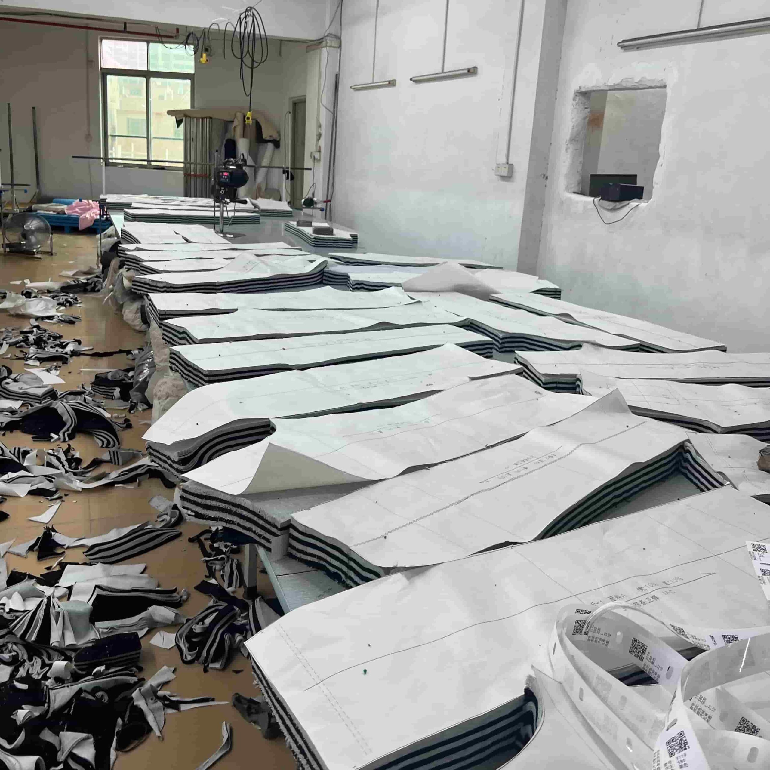Restaurant uniform factory floor showing fabric cutting process with stacked pattern pieces and industrial cutting equipment, demonstrating direct manufacturing without middlemen.