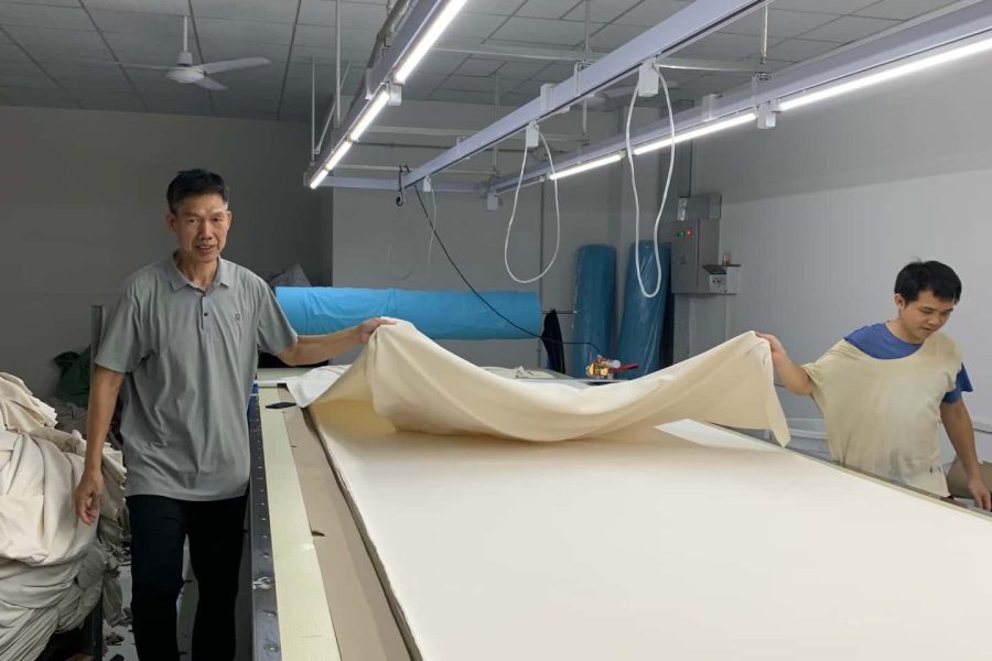 Workers spreading fabric layers on automated cutting table for bulk garment production