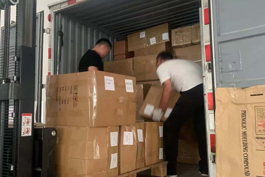 Forklift loading palletized garment cartons onto delivery truck with workers assisting