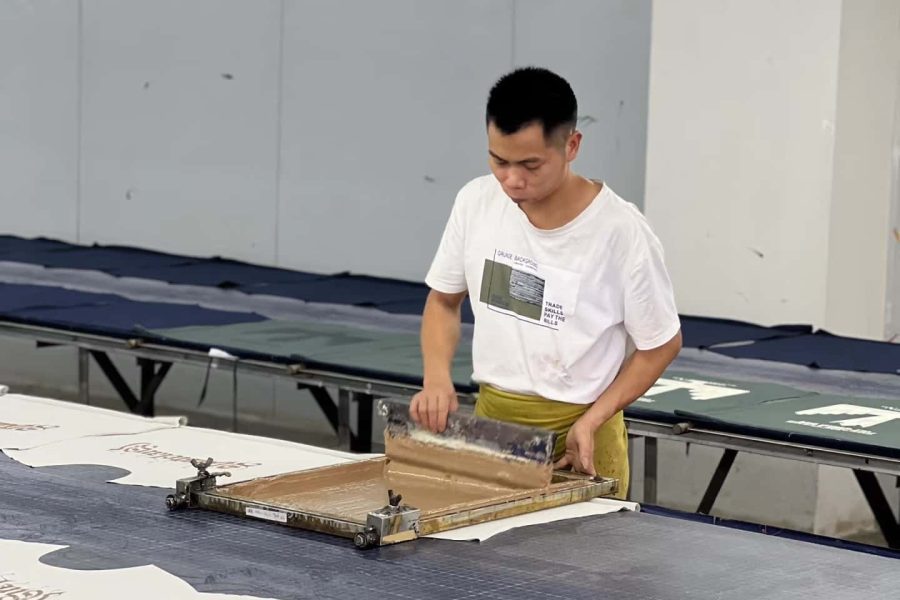 Skilled worker performing manual screen printing on fabric panels at apparel factory